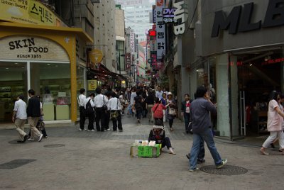 Thursday 10 June, 2010  We wander into the    Myeong Dong    shopping area located behind our hotel. The lady in front of us is selling pancake looking things for about 7¢ Oz money. : Seoul